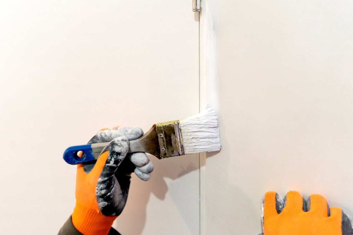 Painter brushing fresh white paint onto an interior door and trim