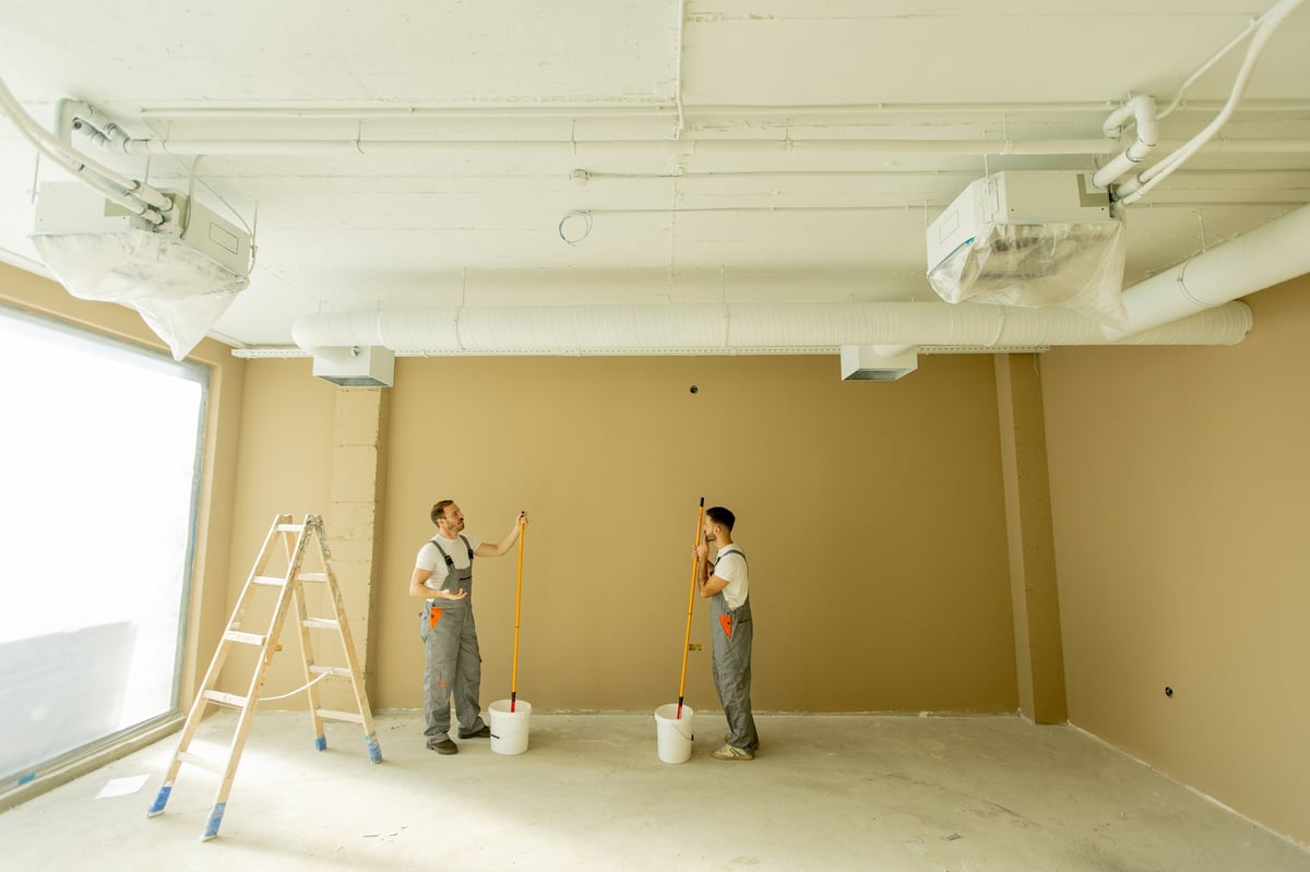 Painters rolling fresh paint onto interior walls of a bright residential room